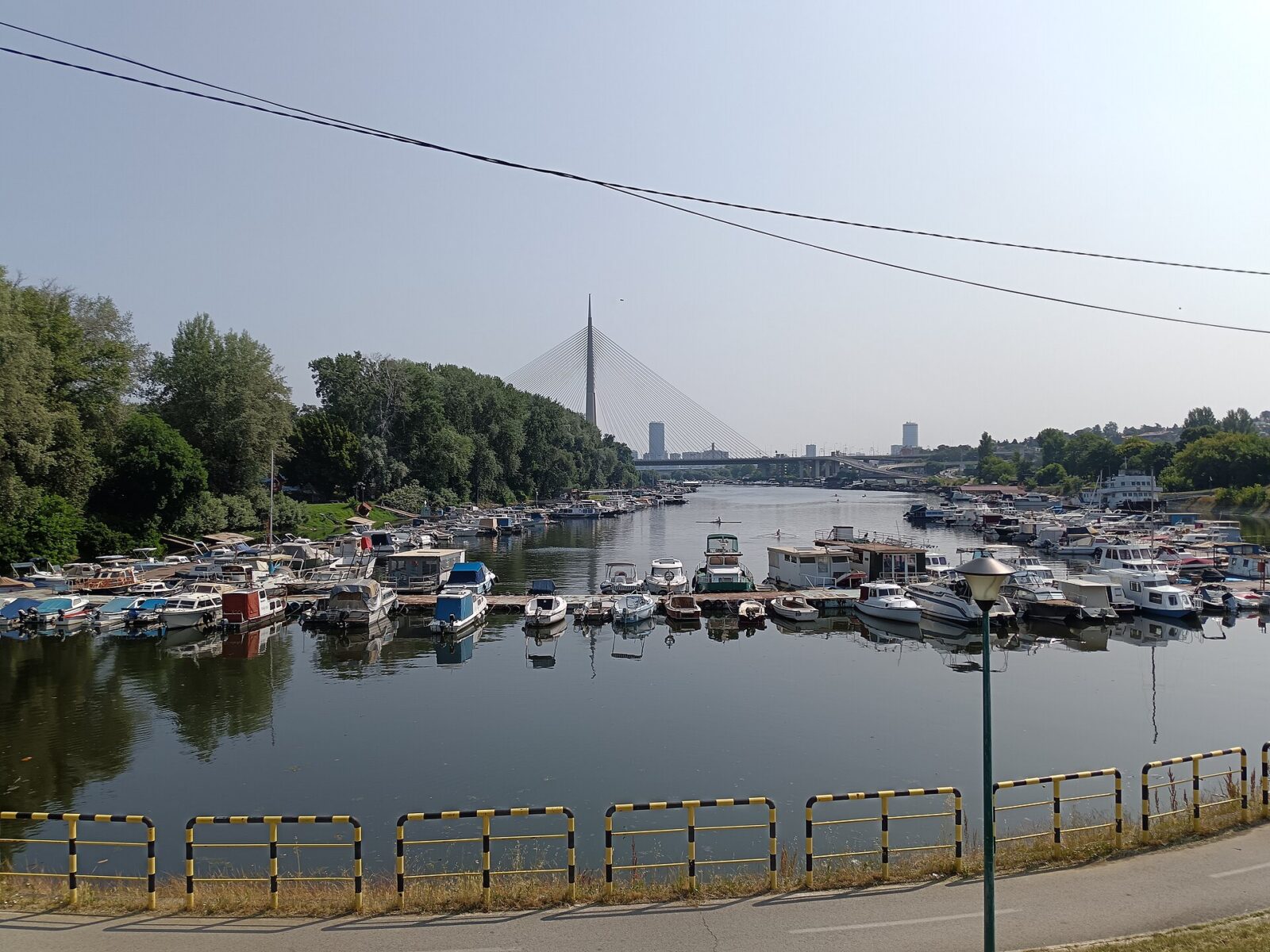 Small boats moored in a marina near Ada Ciganlija, with the Ada Bridge in the background