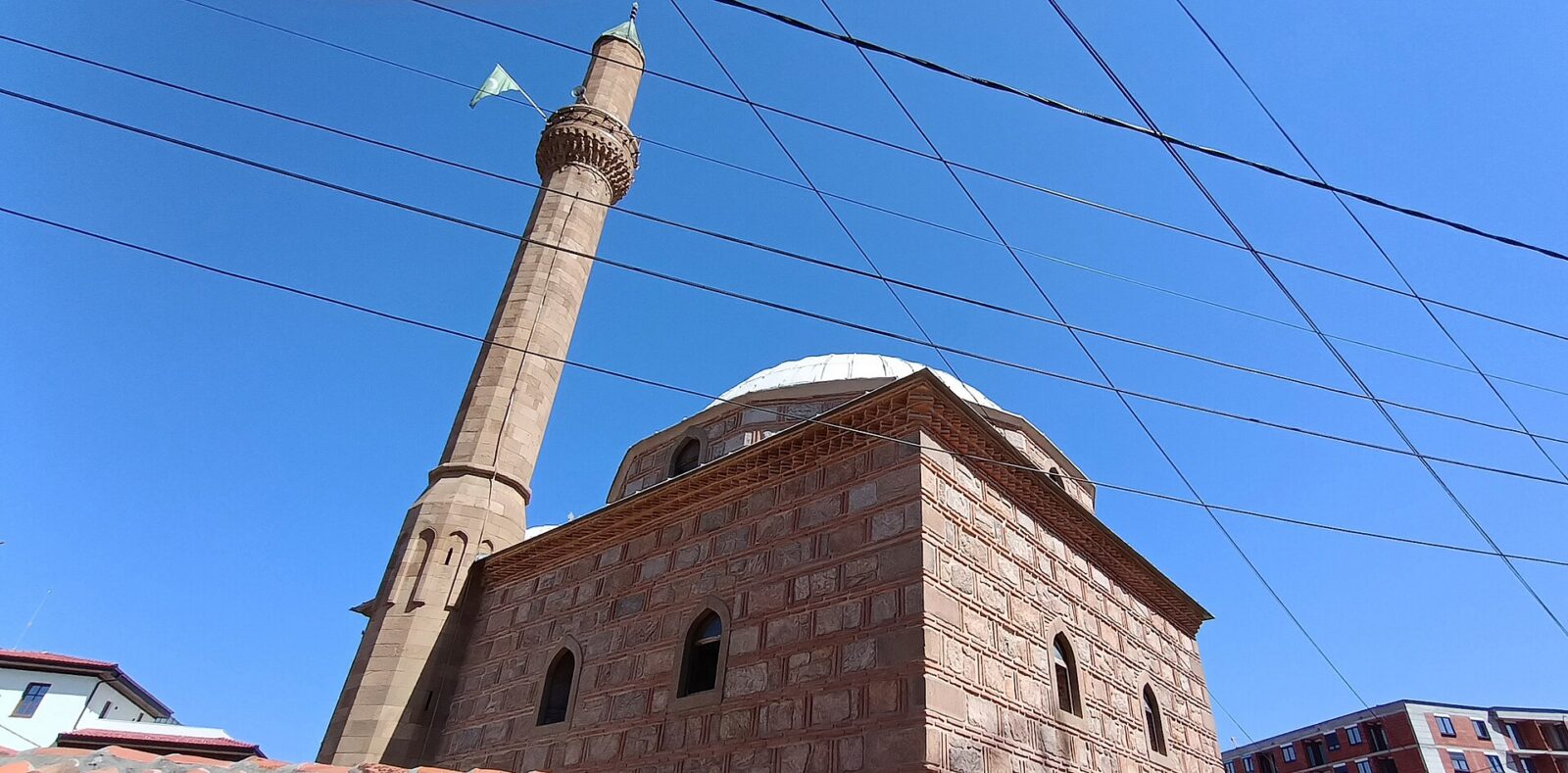 Altun-Alem mosque's stone minaret and domed prayer hall against a clear sky