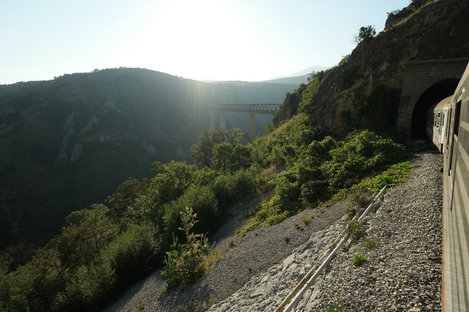 Un treno sulla linea Belgrado-Bar si avvicina a una galleria in una gola montana, con un viadotto visibile più oltre