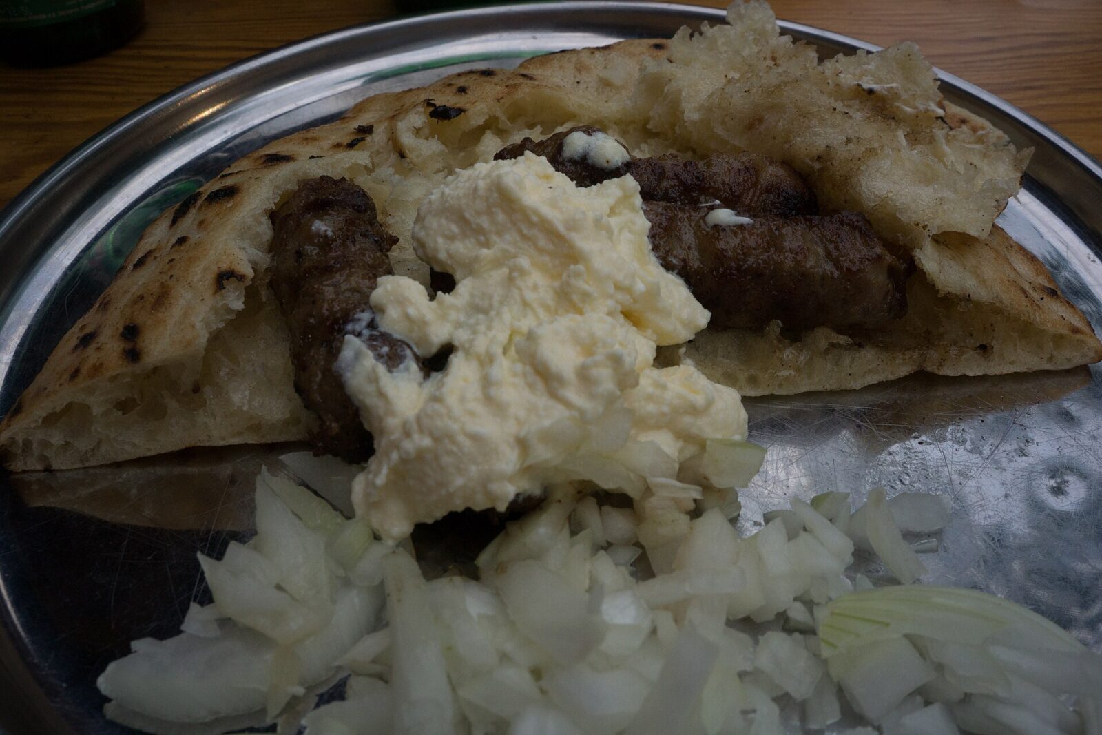 A plate of grilled minced-meat sausages known as cevapi, served with flatbread, chopped onion and kajmak, a popular grilled dish in Serbia