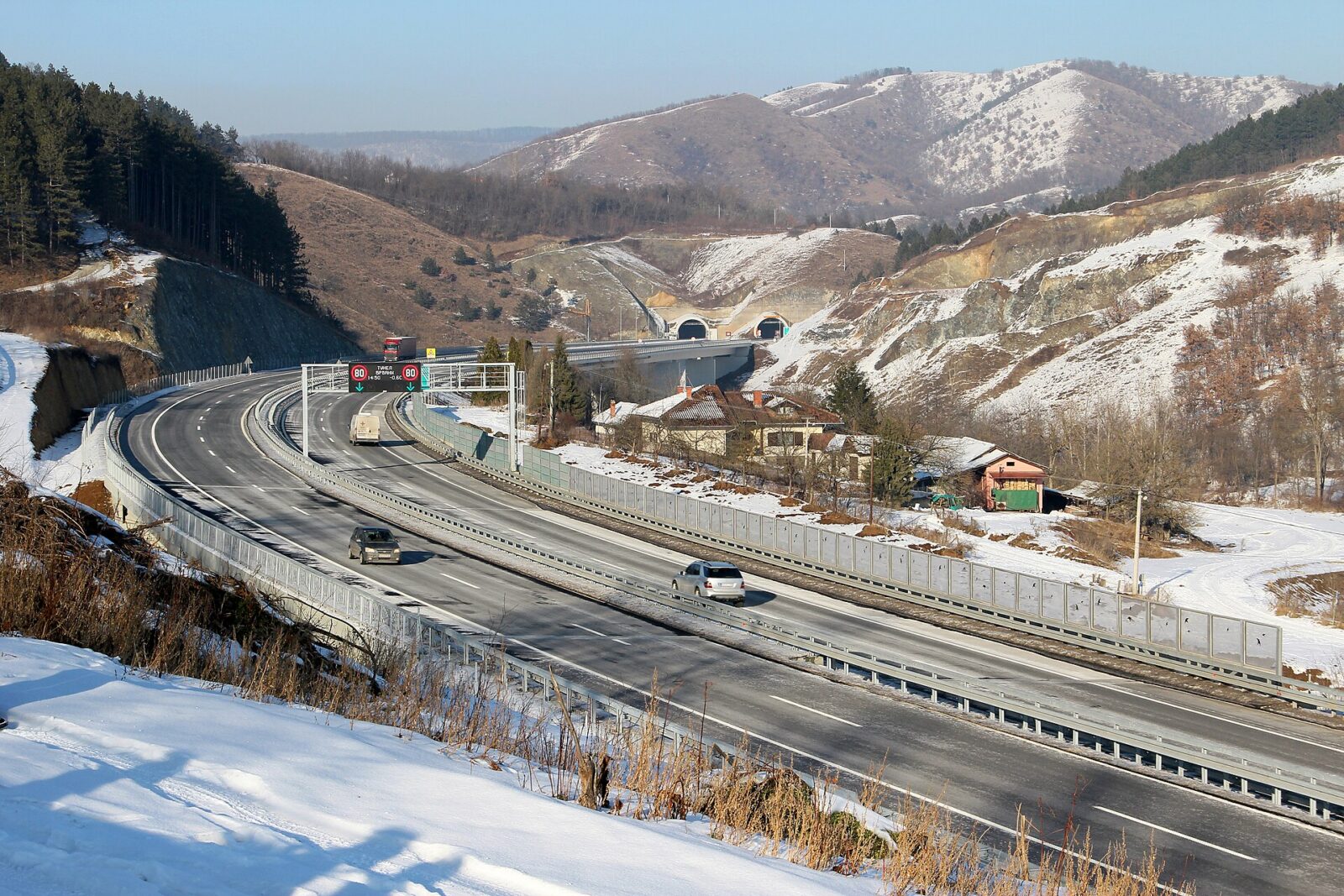A winding motorway through wooded, snow-dusted hills with a tunnel ahead