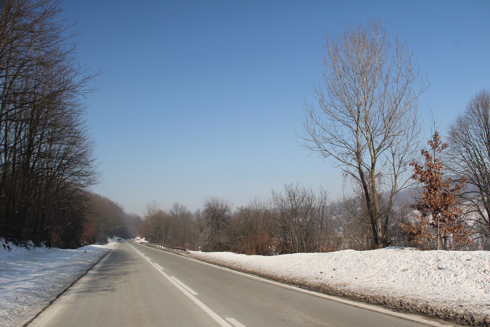 The Ibar valley road running through open countryside, bordered by snow