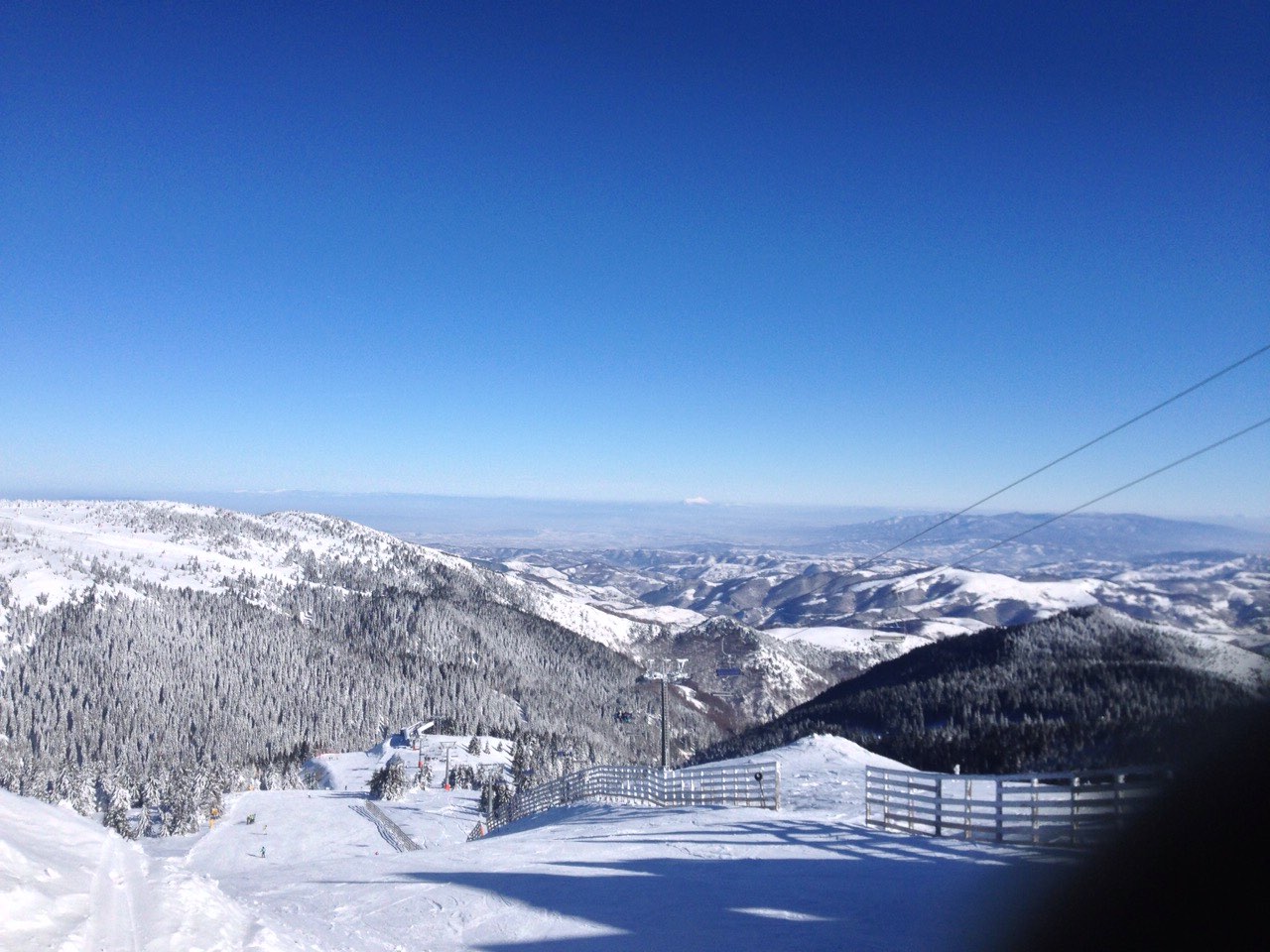 A marked ski run at Kopaonik descending toward a forested valley under a clouded sky