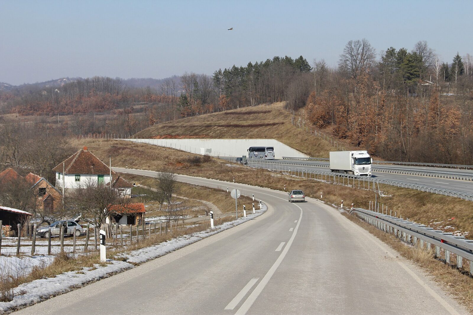 Trucks and cars passing along a rural stretch of the Miloš Veliki motorway, with a village nearby