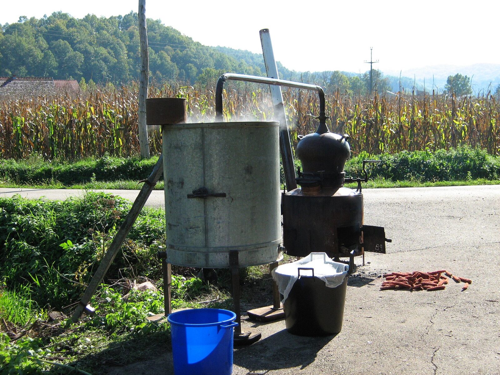 A small copper still set up for home rakija production, beside a cornfield