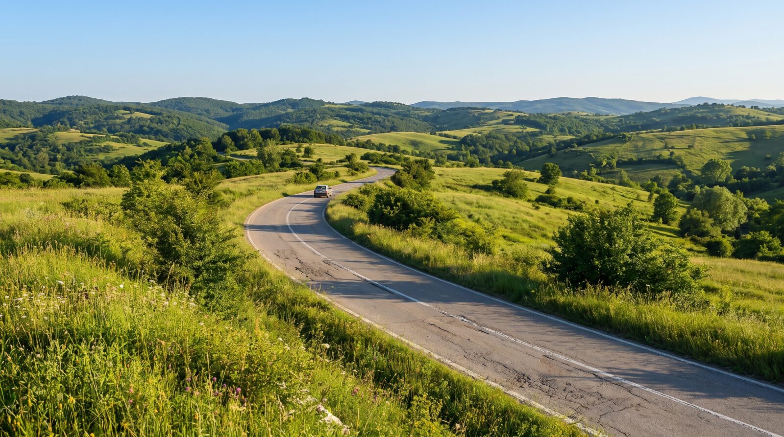 A car travels a winding two-lane road through green rolling hills in western Serbia