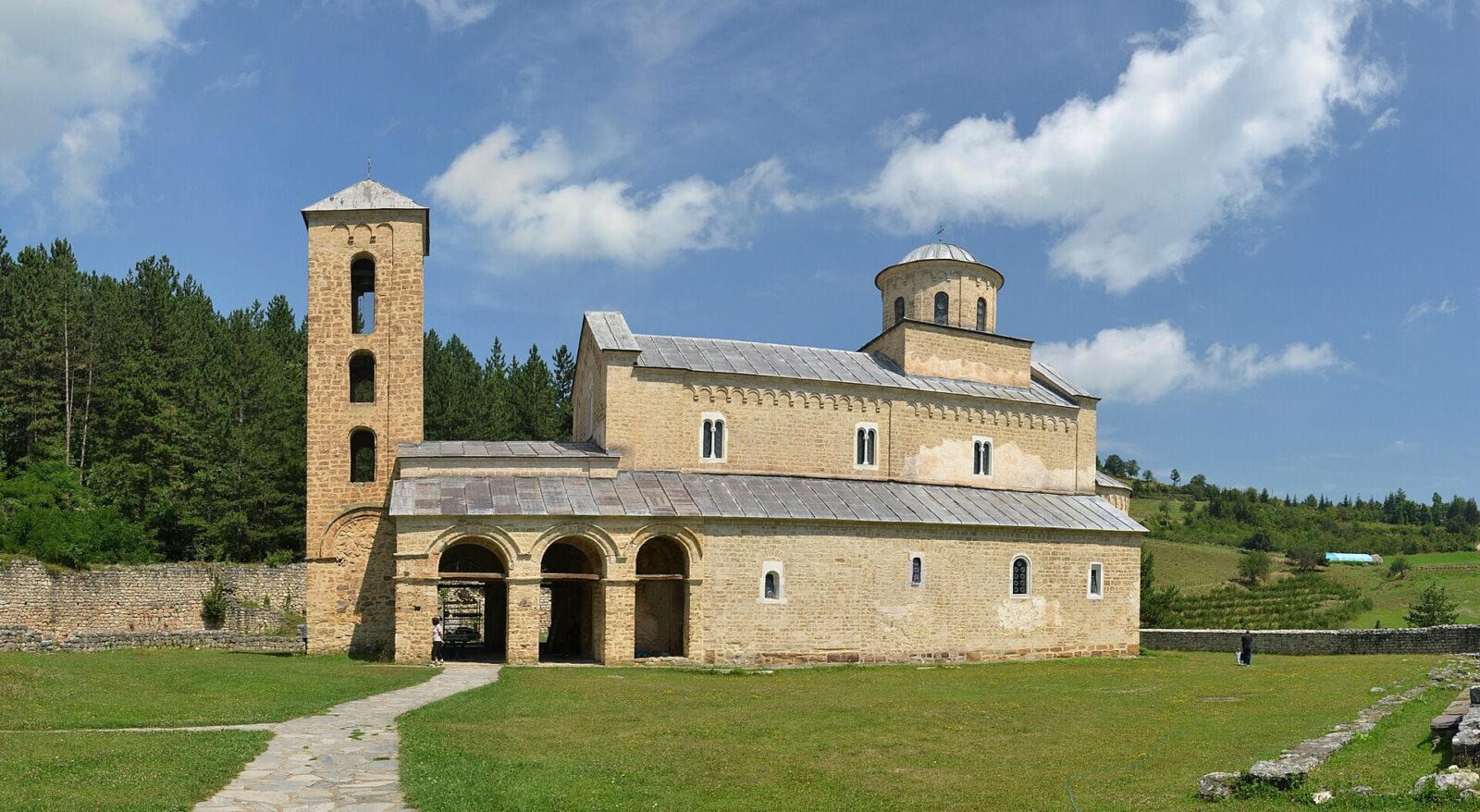 Sopocani monastery church and bell tower, set in an open grassy clearing bordered by forest